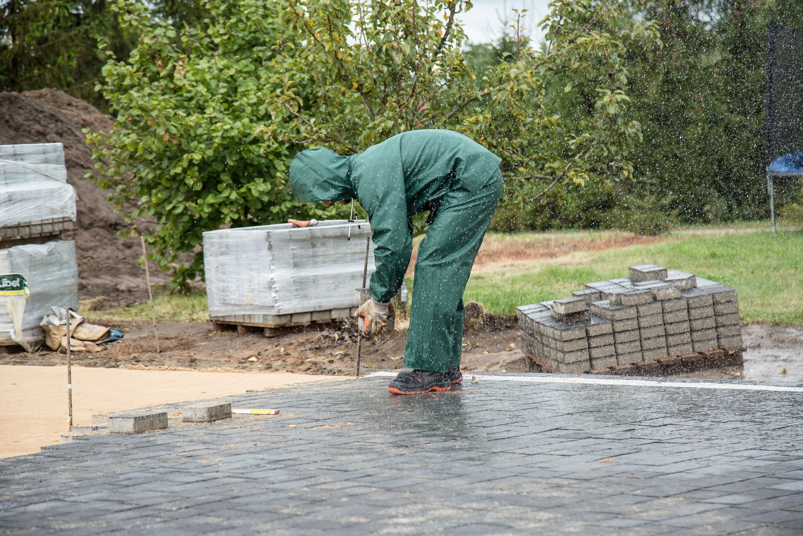 A landscaper in work overalls laying block paving to line and level on a fresh sand bed