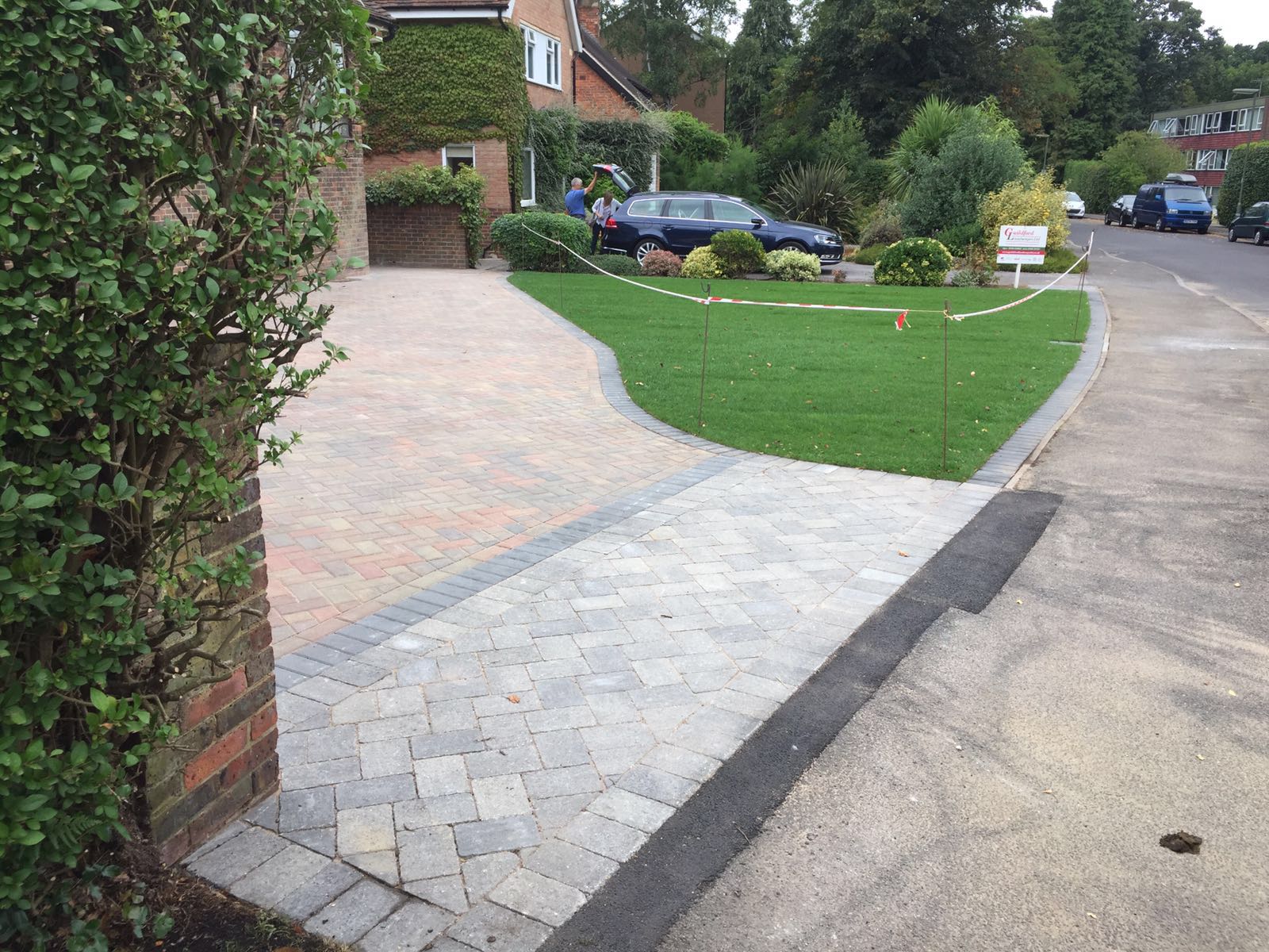 Natural riven paving being laid to line and level over a sand bed, held by a timber-sleeper retaining edge against the planted border.