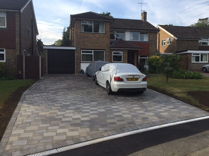 A grey block-paving driveway finished with a full-width drainage channel at the threshold — the kind of detail that keeps water off the house.