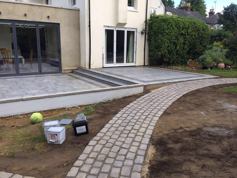 A porcelain terrace with a stepped level change linking bi-fold doors to the garden, with a hand-laid cobble path curving away across the plot.