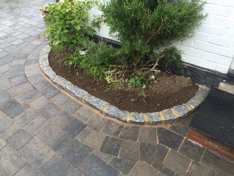 A curved granite-sett edging course setting off a fresh planting bed, tying the block paving and the brickwork of the house together.